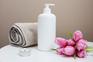 A white pump bottle, a rolled towel, a tealight candle, and pink tulips on a table.